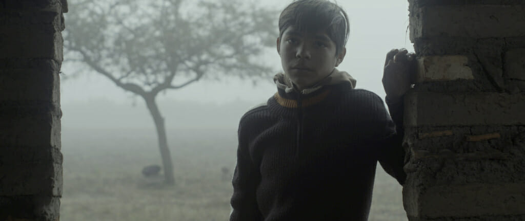 film still showing a child under a brick doorway against a foggy background