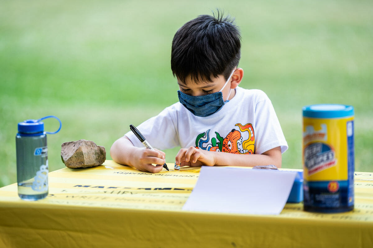 child writing on a strip of plastic on a table