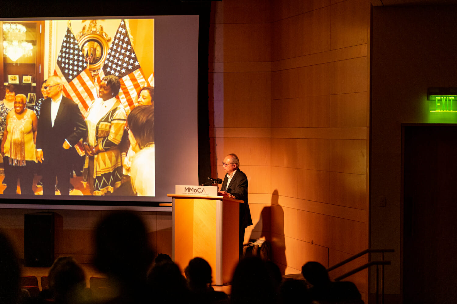 Mel Chin speaking into a microphone at the podium during his lecture