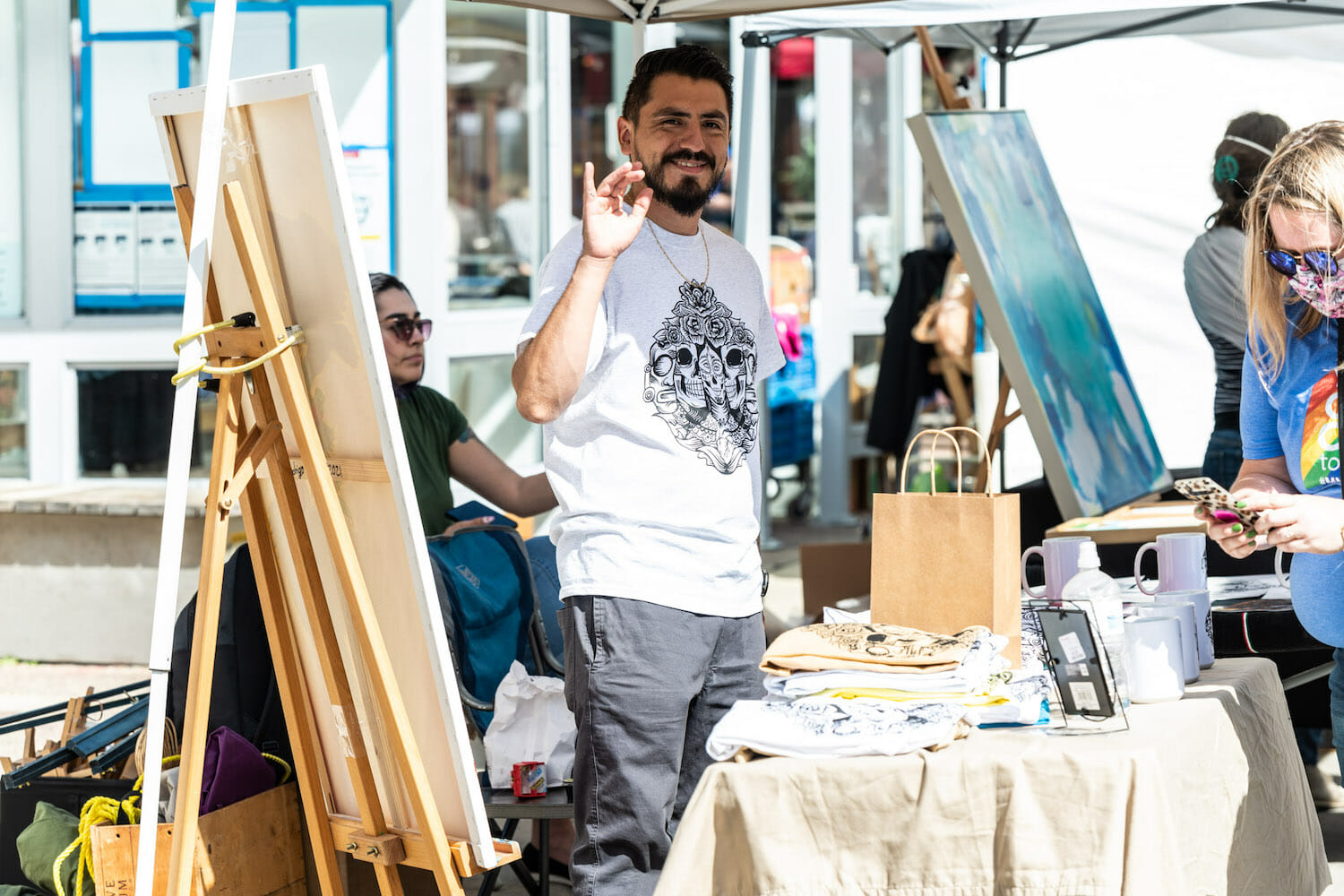 artist at Art Fair on the Square at their booth surrounded by paintings, waving at the camera