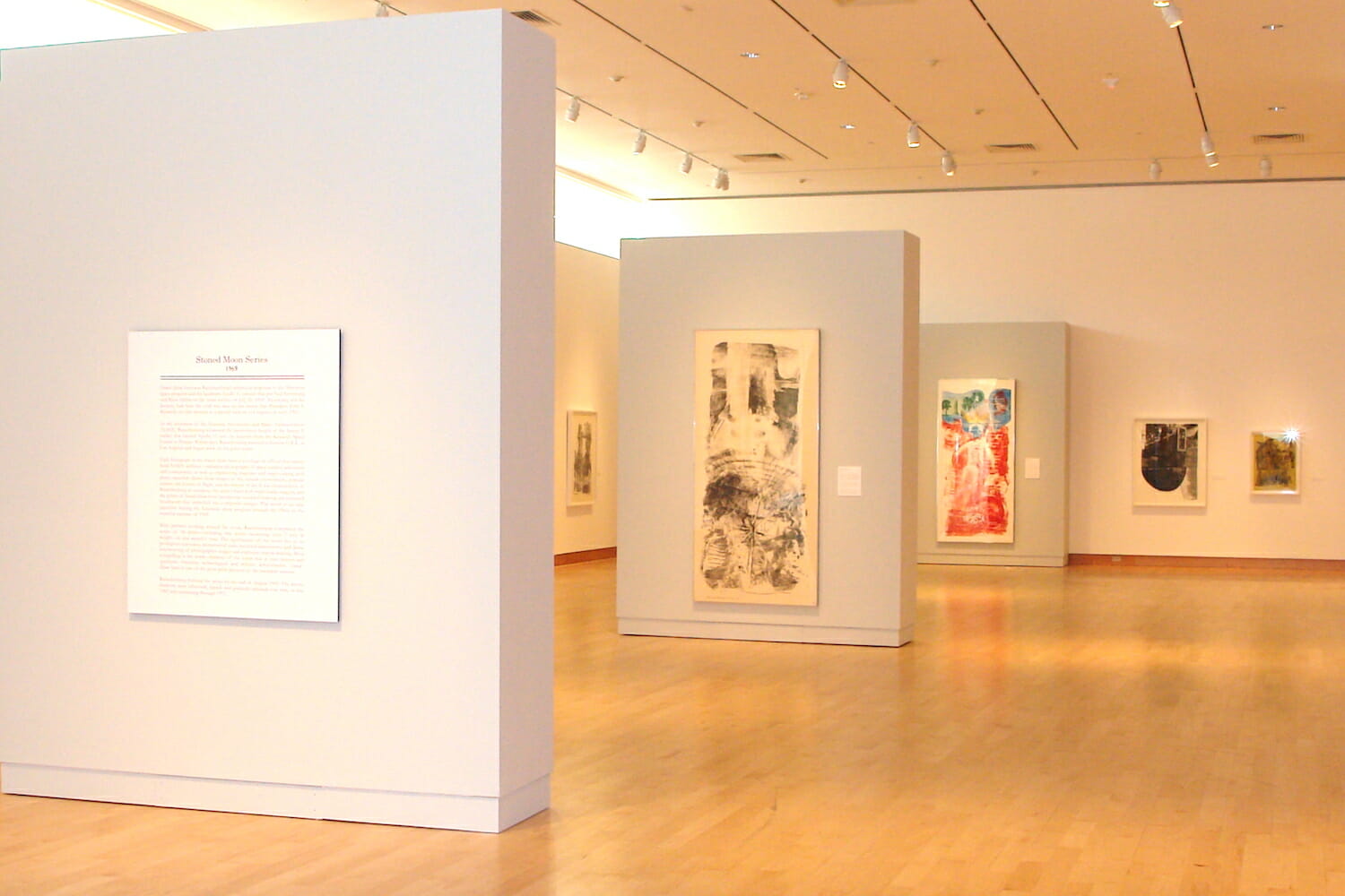 installation view of "Signs of the Times: Robert Rauschenberg's America" featuring wall text and artworks hanging on the wall