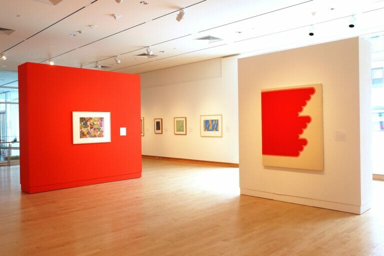 installation view of an exhibition with framed artworks hung in a row and artworks on a wall