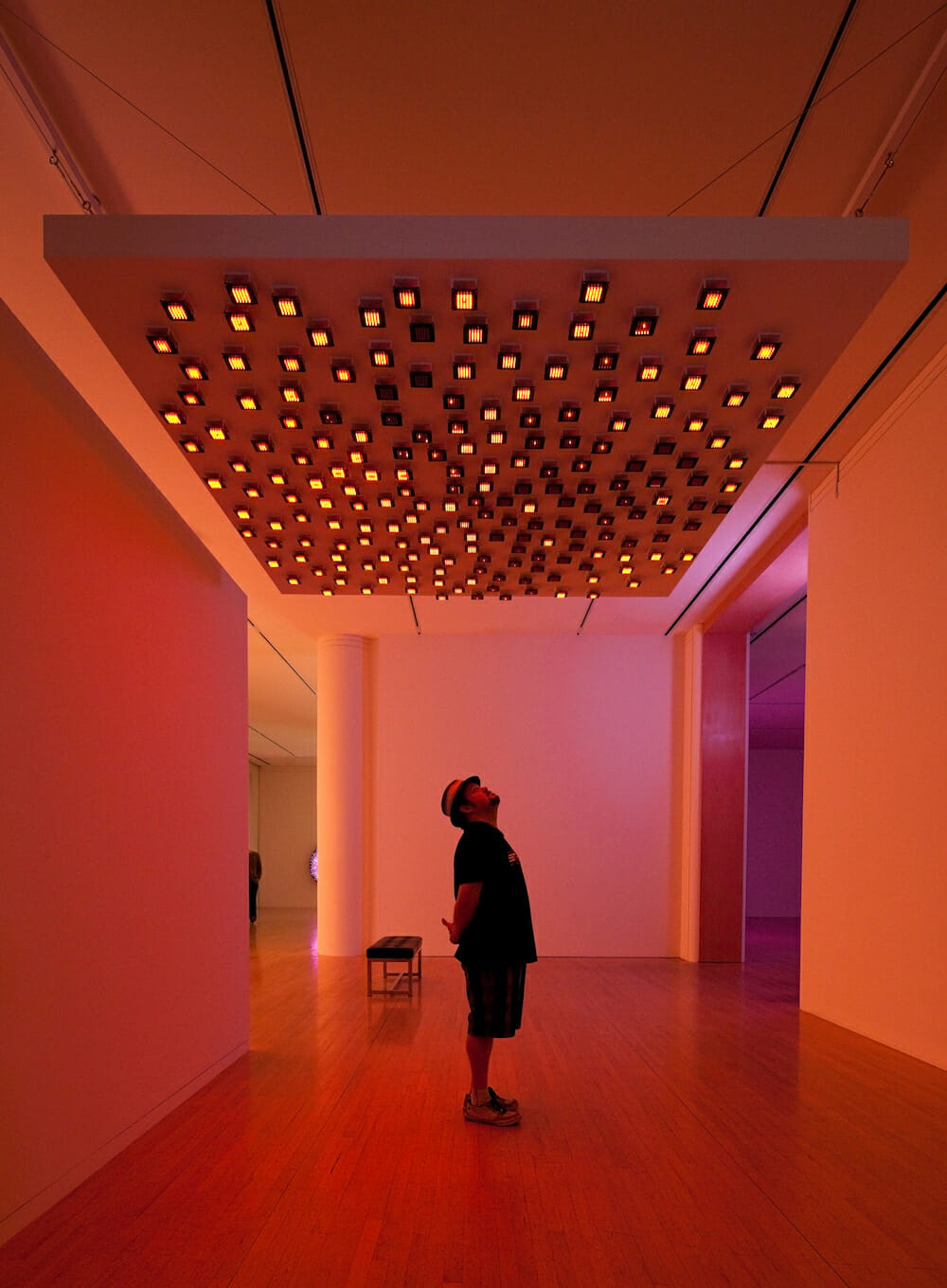 installation view of "Leo Villareal" showing a visitor standed in a darkly lit room with light artworks hanging from the ceiling