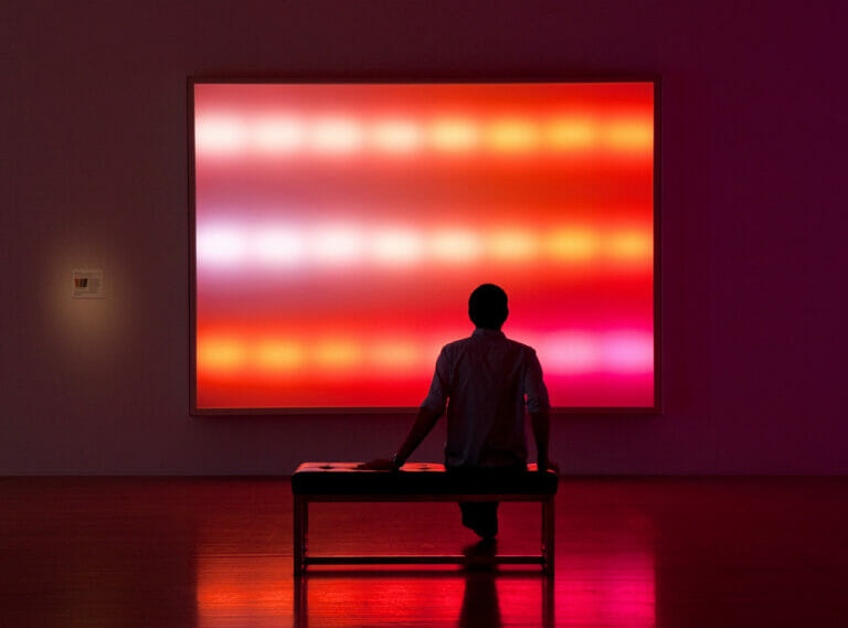 installation view of "Leo Villareal" showing a seated visitor in a darkly lit room with light artwork on the wall