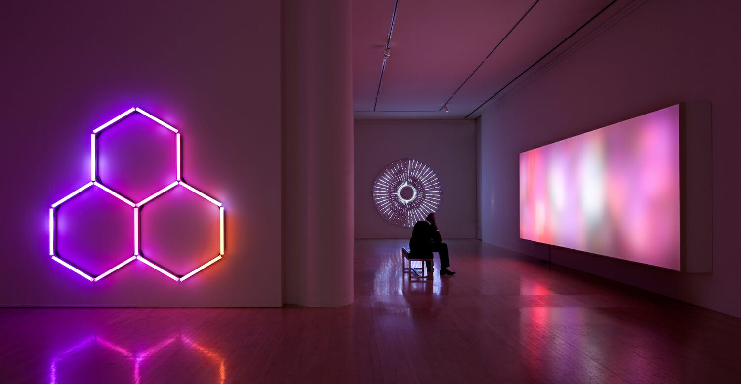 installation view of "Leo Villareal" showing a seated visitor in a darkly lit room with light artworks on the walls