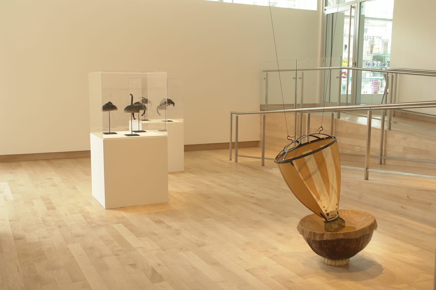 installation view of the exhibition Altered Geometry, featuring an abstract sculpture resembling a spinning top and two vitrine display cases with smaller sculptures resembling African American hairstyles