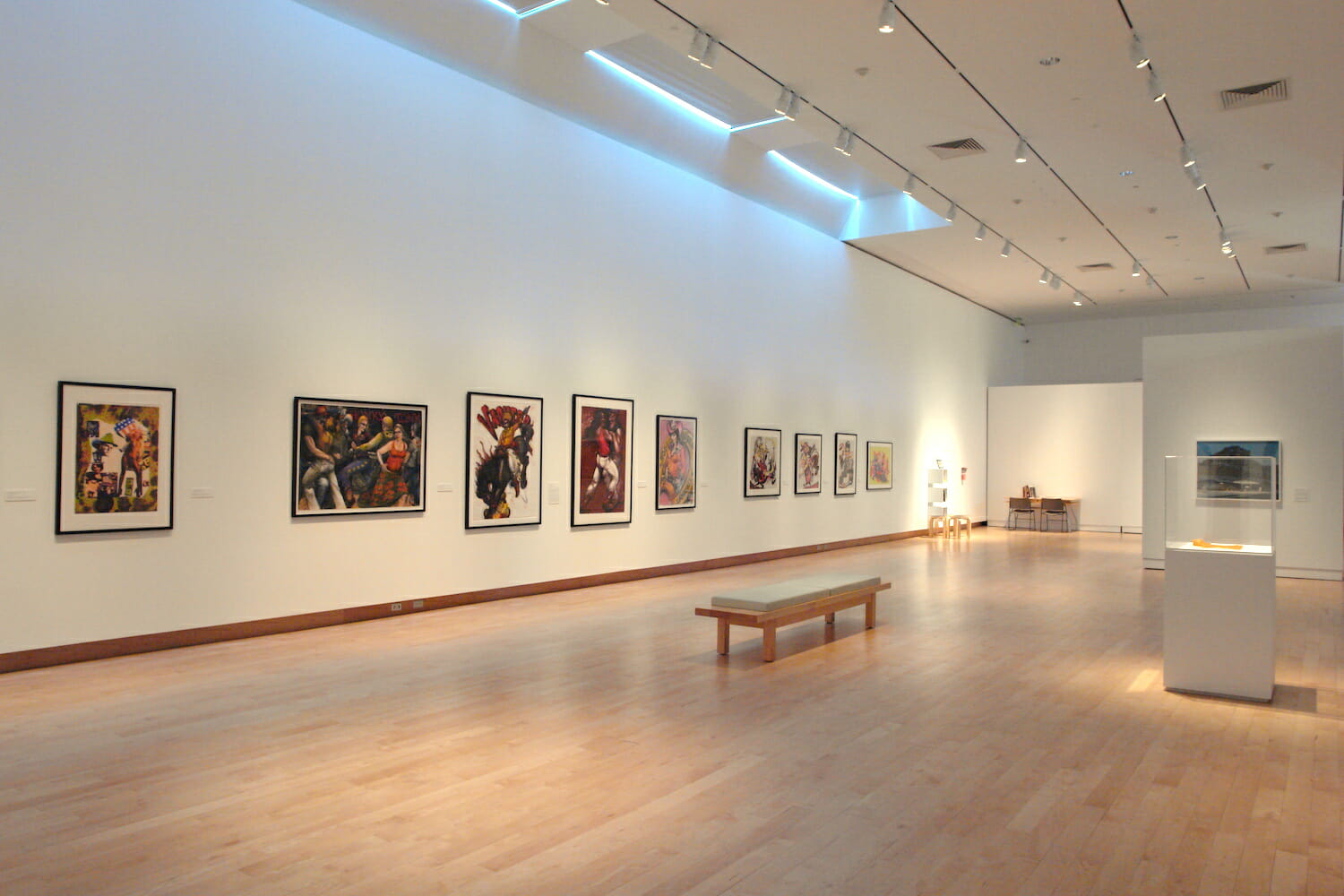 installation view of the exhibition titled Apple Pie featuring artworks hanging vertically across a long wall, with a long bench in the middle of the room and vitrine display cases