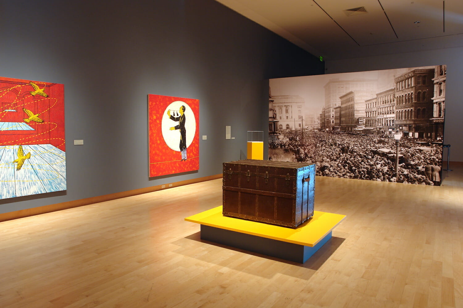 installation view of Houdini: Art and Magic featuring artworks and vinyl images on walls and a trunk on a platform