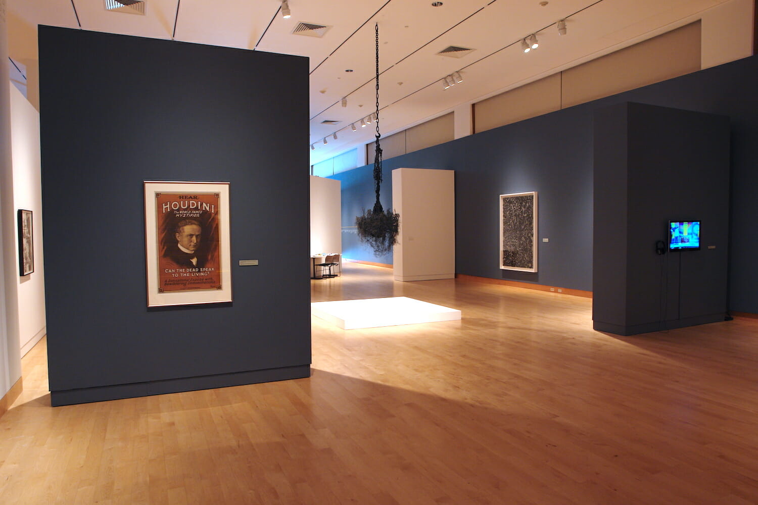 installation view of Houdini: Art and Magic featuring framed artworks, a screen, and a hanging artwork