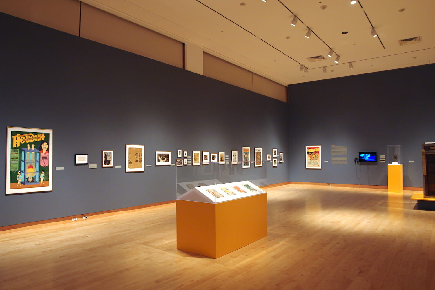 installation view of Houdini: Art and Magic featuring framed artworks and a long vitrine display case