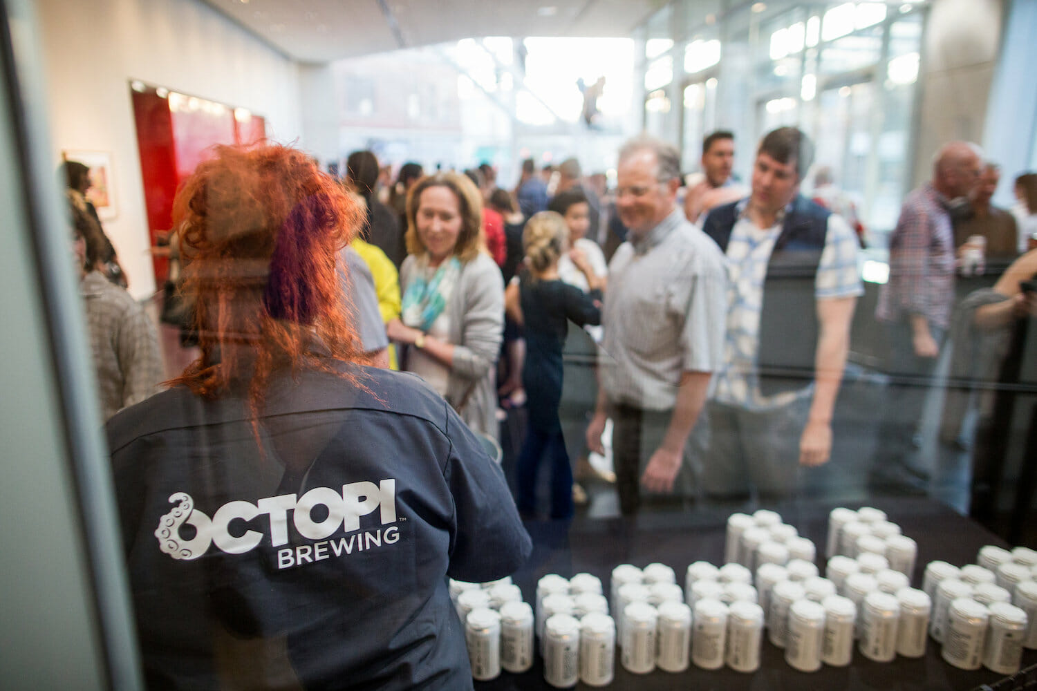 employee from Octopi Brewing serving cans of beer to the public in a room full of people