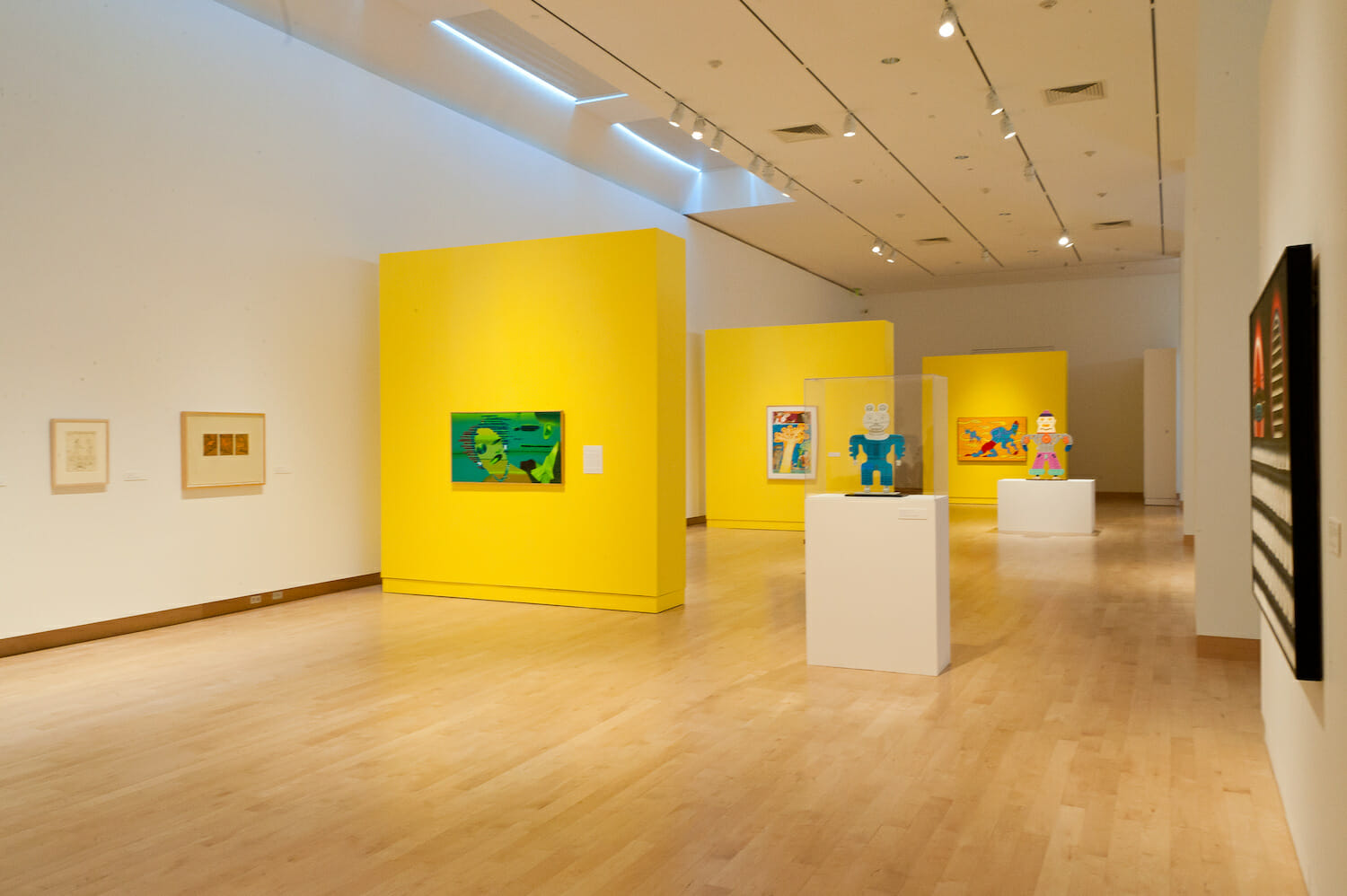 gallery installation view of the exhibition Chicago Imagists. there are two vitrine display cases or platforms with various artworks or objects. artworks hang on the nearby walls.