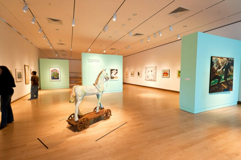 installation view of the exhibition Chicago School featuring a horse sculpture surrounded by artwork hanging on walls and two people looking at artworks