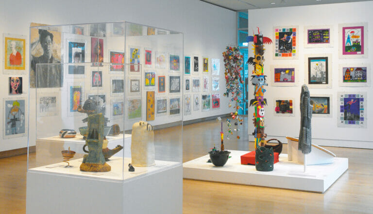 gallery installation view of Young at Art 2009, featuring sculptures on low platforms and inside glass vitrines and artworks displayed on the walls