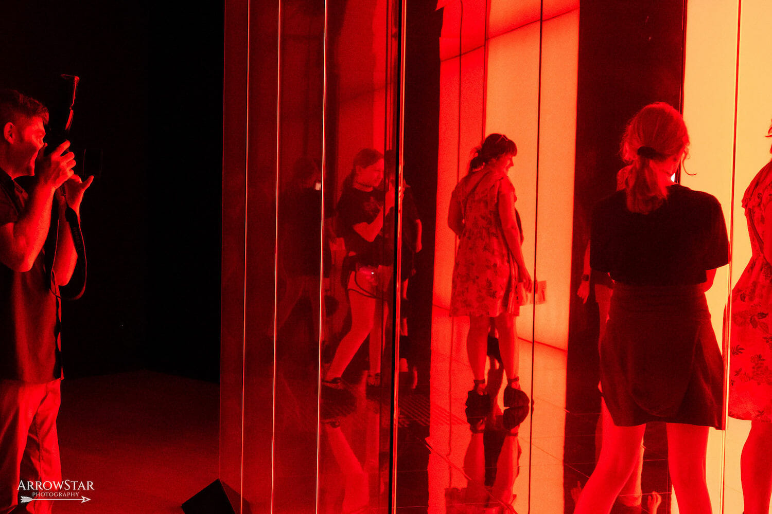 installation view of Garden of Eden by Faisal Abdu'Allah, featuring at least five people walking through the interactive space with a red glow