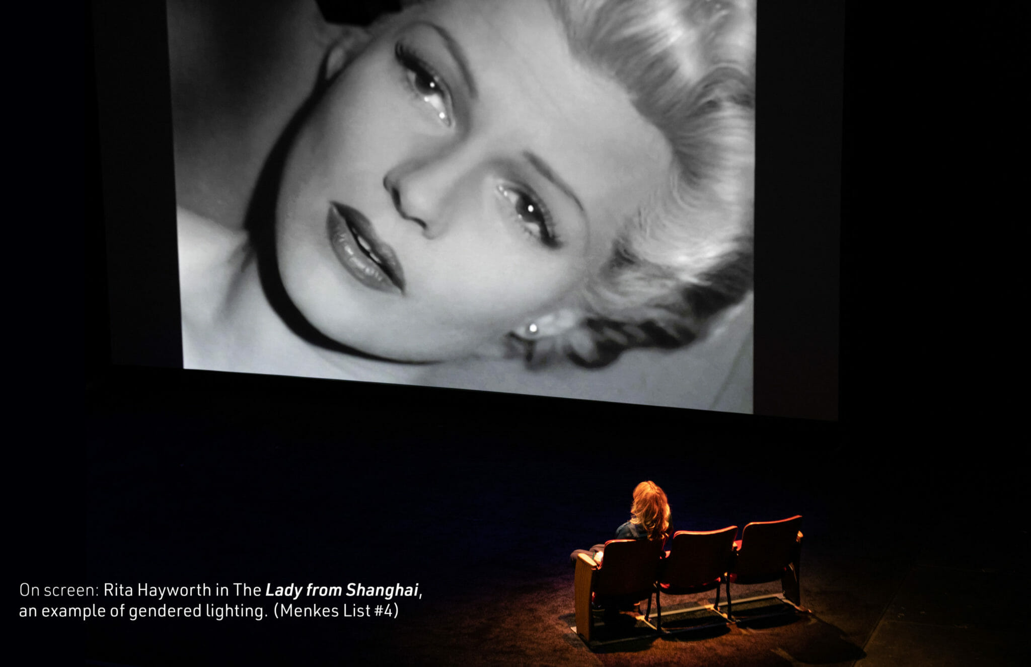 three chairs, one occupied by a person who looks at a projected screen showing Marilyn Monroe