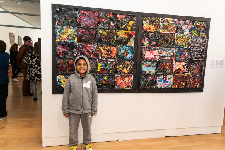 A child artist standing in front of a large abstract artwork.