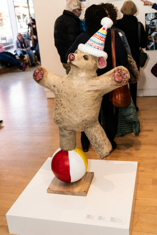 Sculpture of a circus bear standing on a beach ball with a party hat.