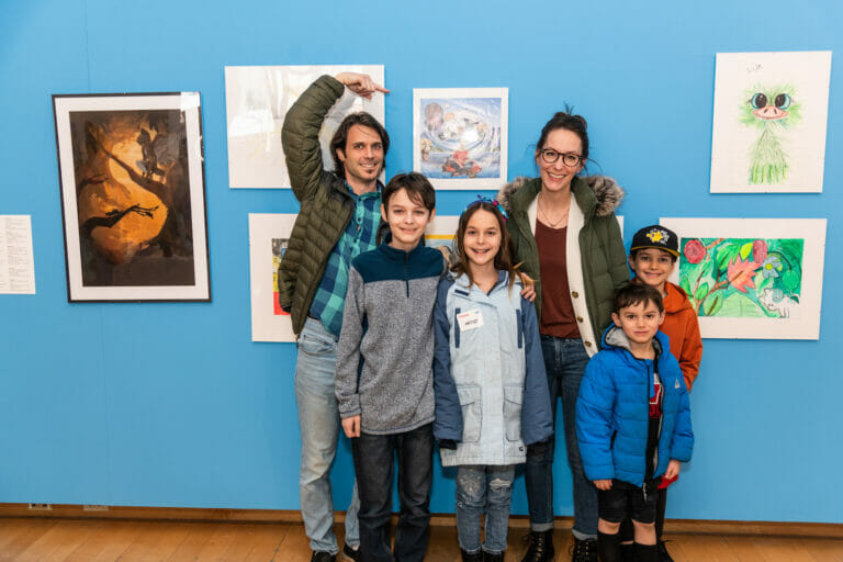 A family and a child artist poses for a photo while one person points at a child's artwork.