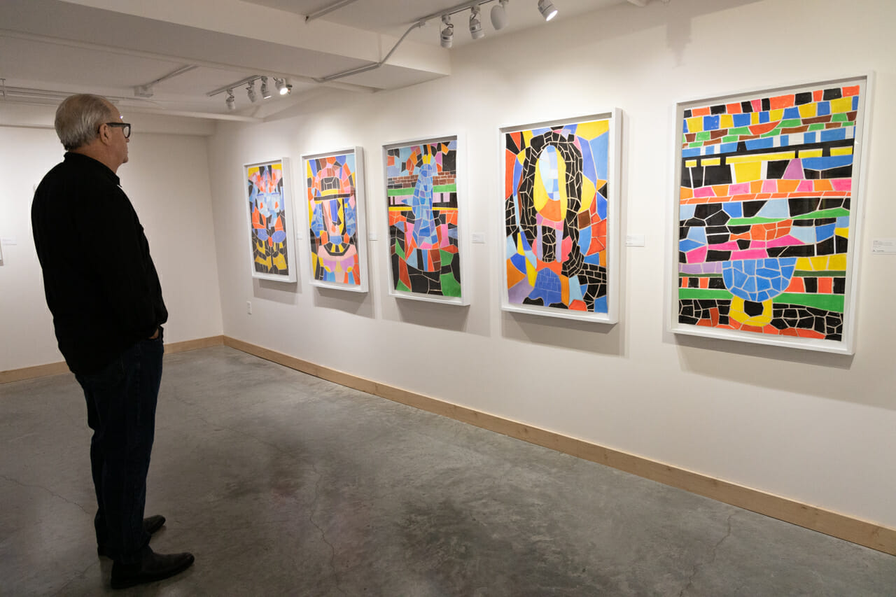 A person standing in front of five large art canvases hanging on a gallery wall.