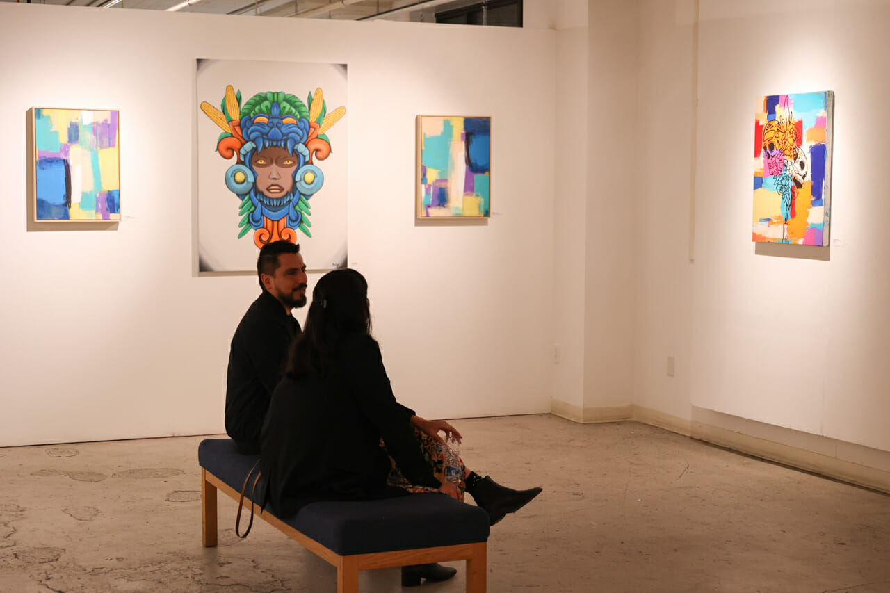 Two people seated on a bench in an art gallery.