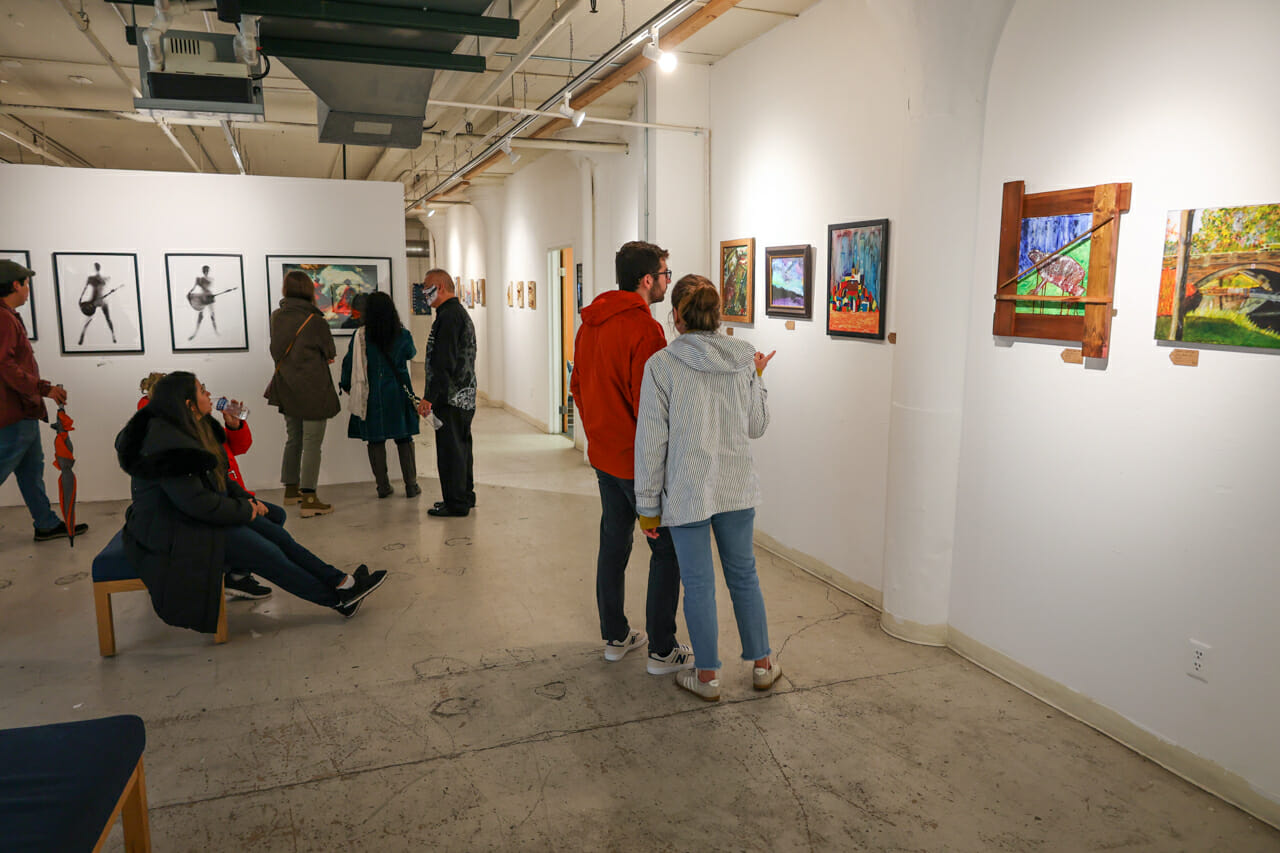 People standing or seated in a gallery while looking at artwork.