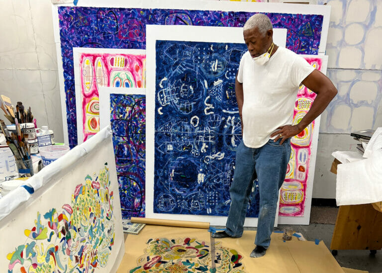 Artist Floyd Newsum standing in his studio, surrounded by his paintings.