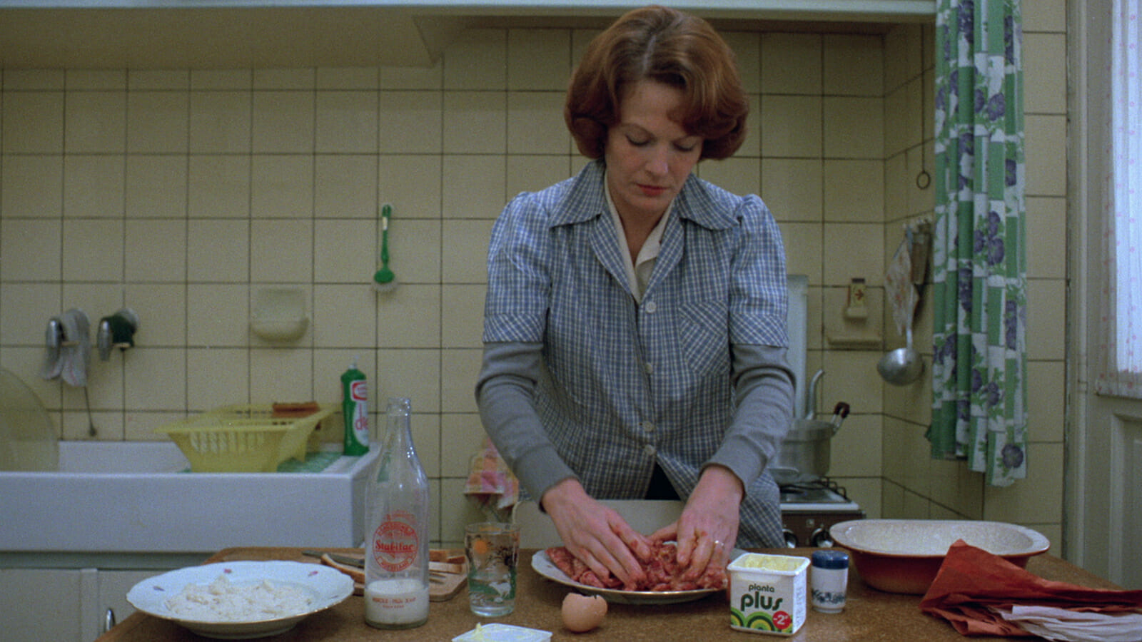 Film still depicting a woman preparing food in a kitchen.