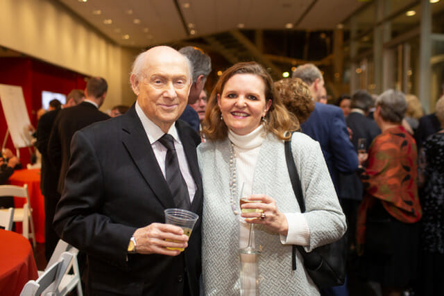 Two people at an exhibition opening are standing next to each other, smiling for the camera.