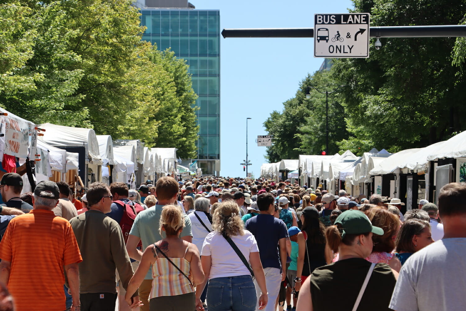 Crowds of people walking between rows of art fair booths at Art Fair on the Square.