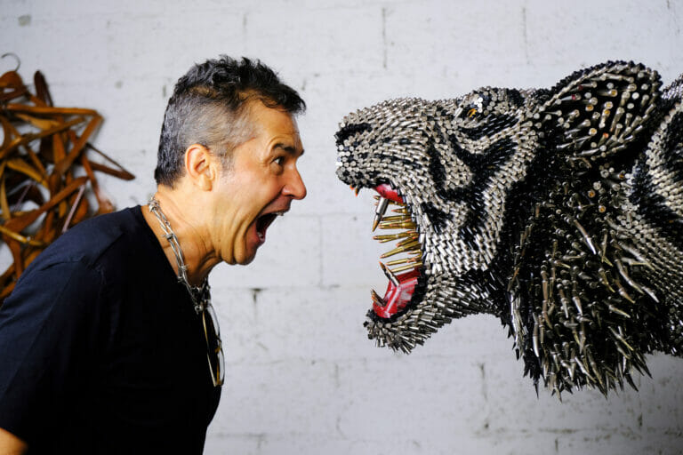 Artist Federico Uribe pretending to scream at their sculpture of a feline animal.