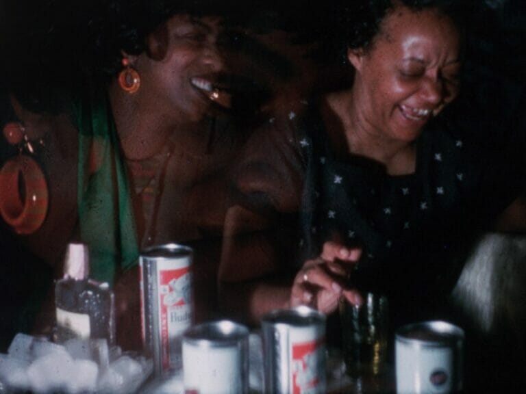 Two laughing figures seated at a table with alcohol containers.