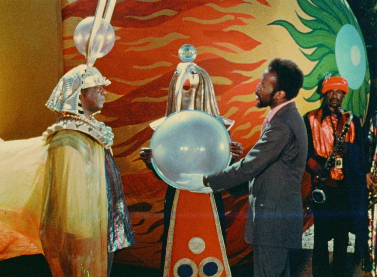 A person on the right handing over a crystal ball to the other person on the left with costumes on.